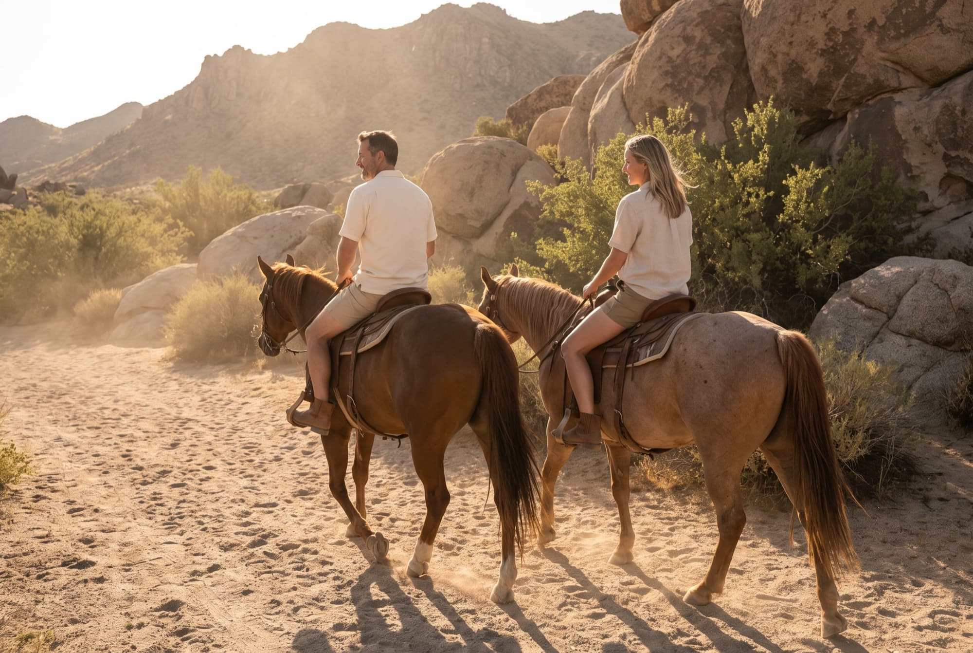 Two guests riding horses side by side through the desert at golden hour