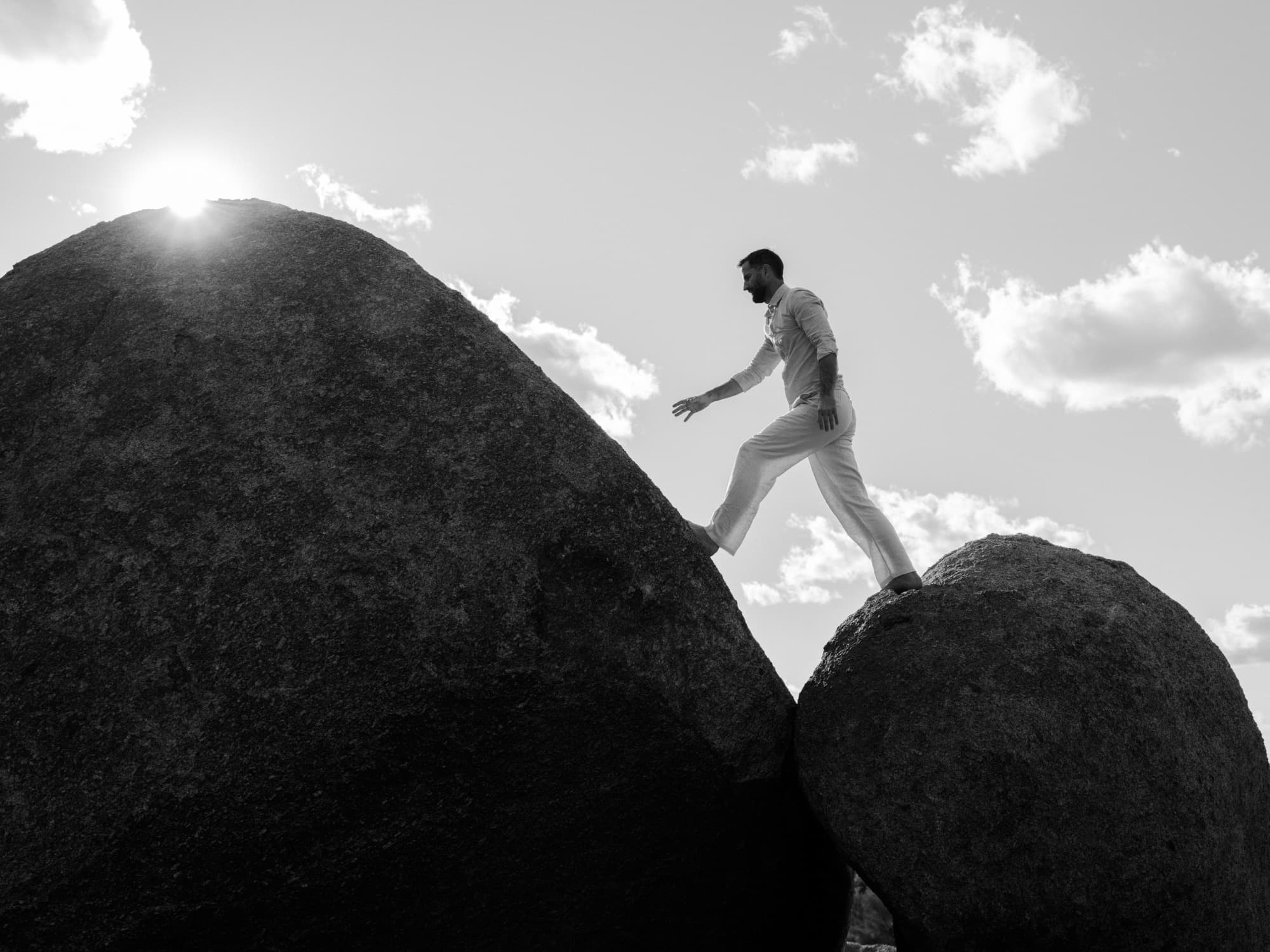 A man stepping between two granite boulders with the sun flaring behind