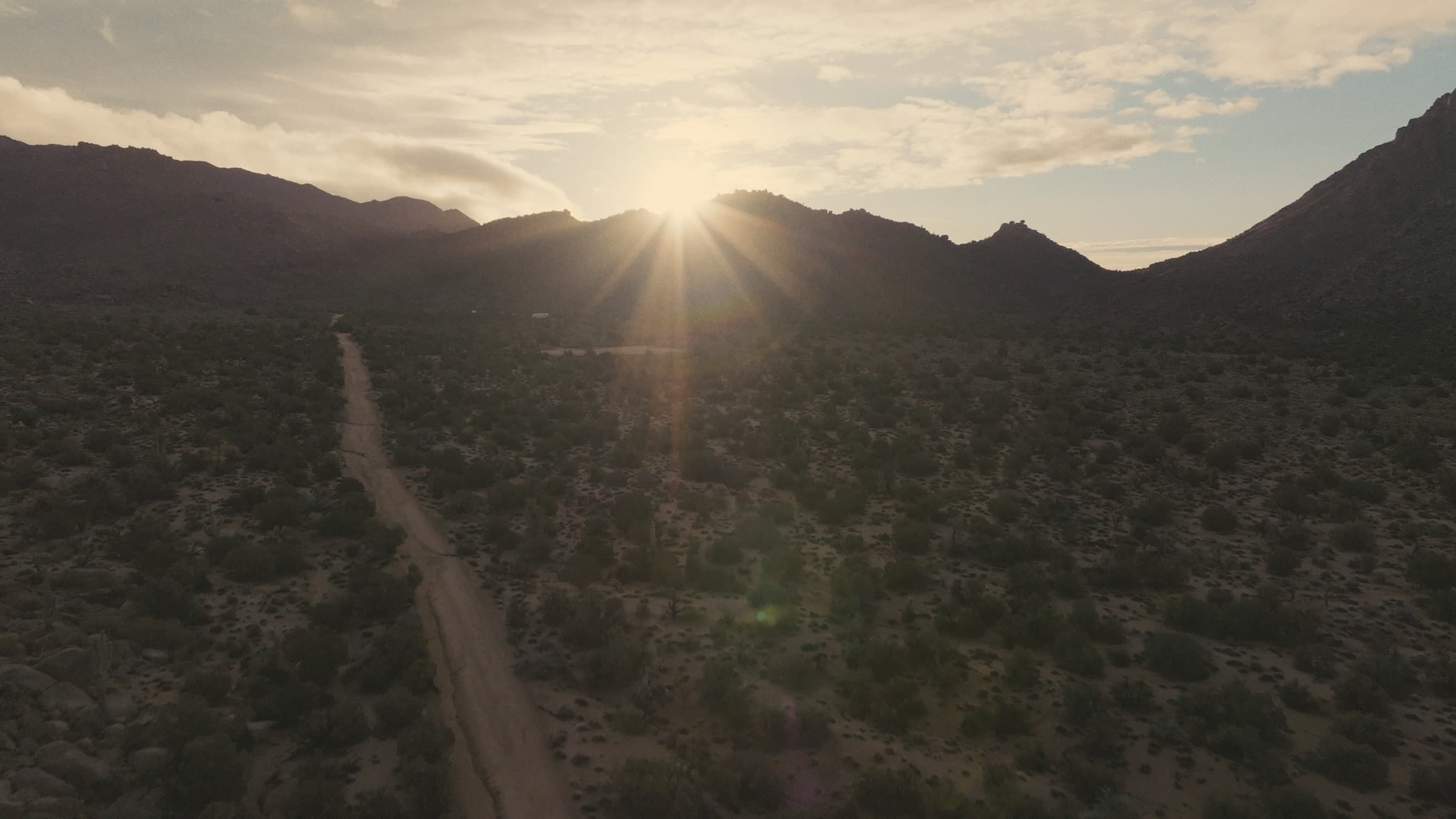 The desert track running toward the mountains with the sun breaking over the ridge