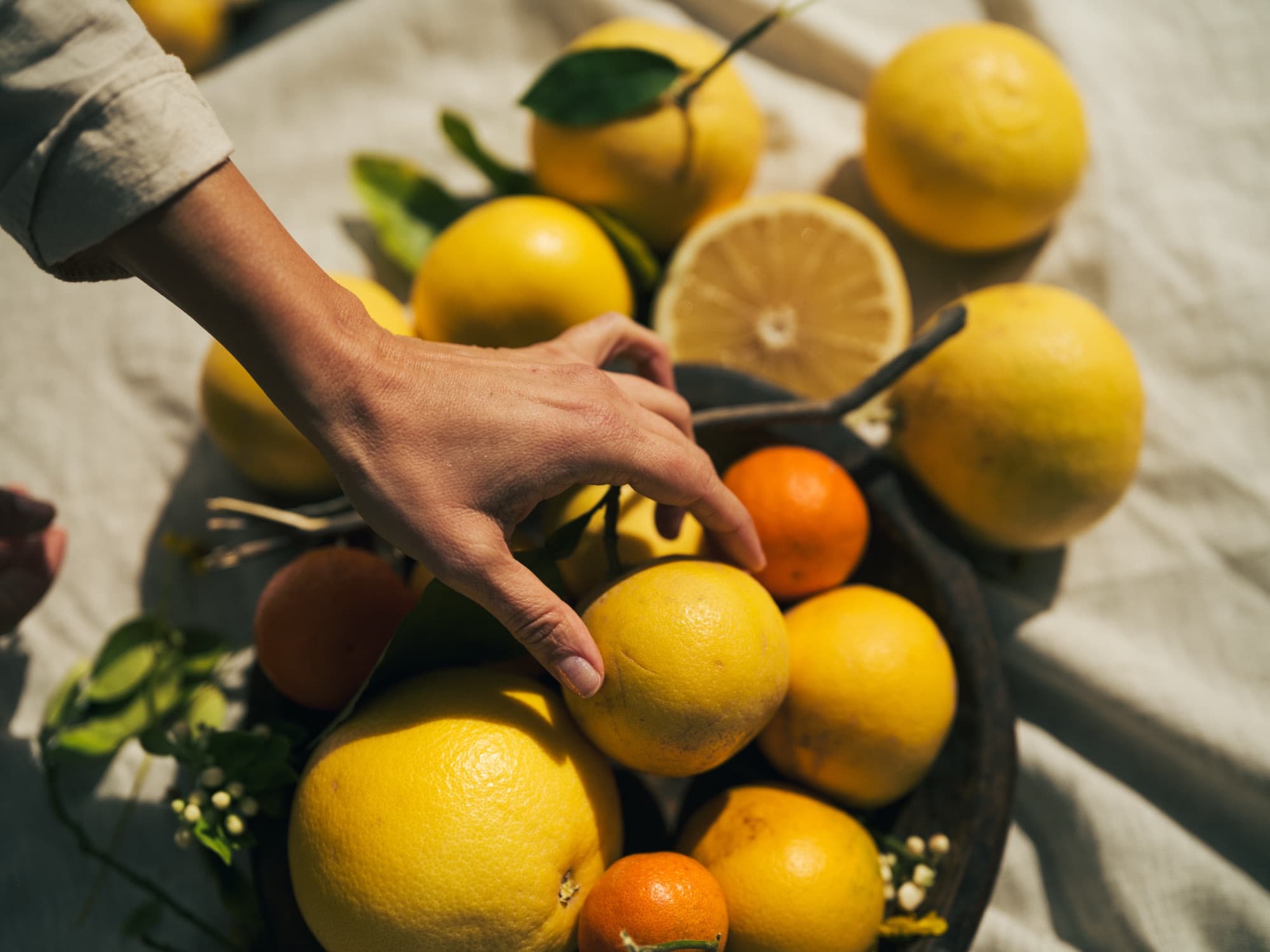 A hand reaching into a bowl of just-picked citrus