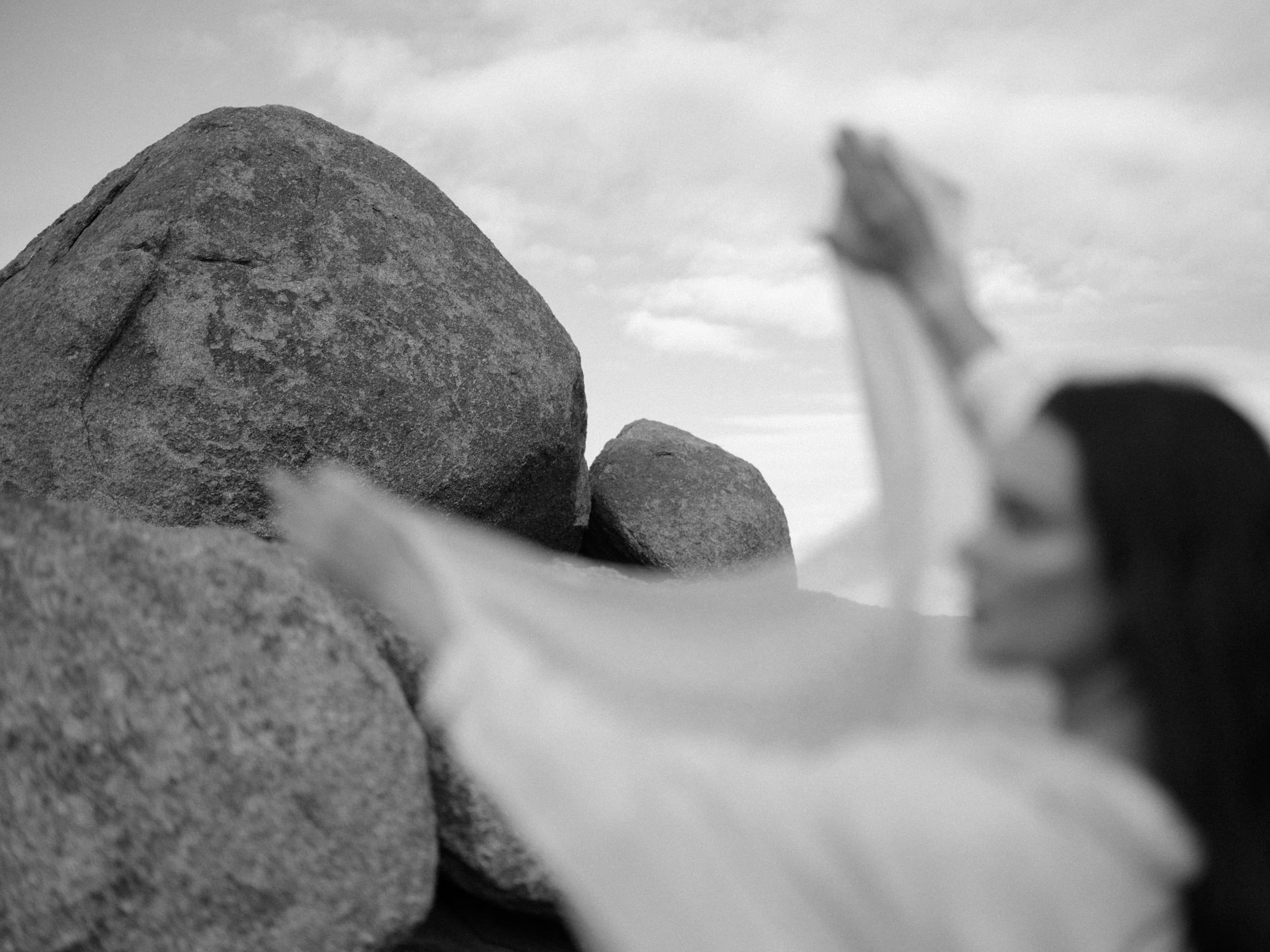 A woman in flowing white raising her arms beside the granite boulders of Box Canyon