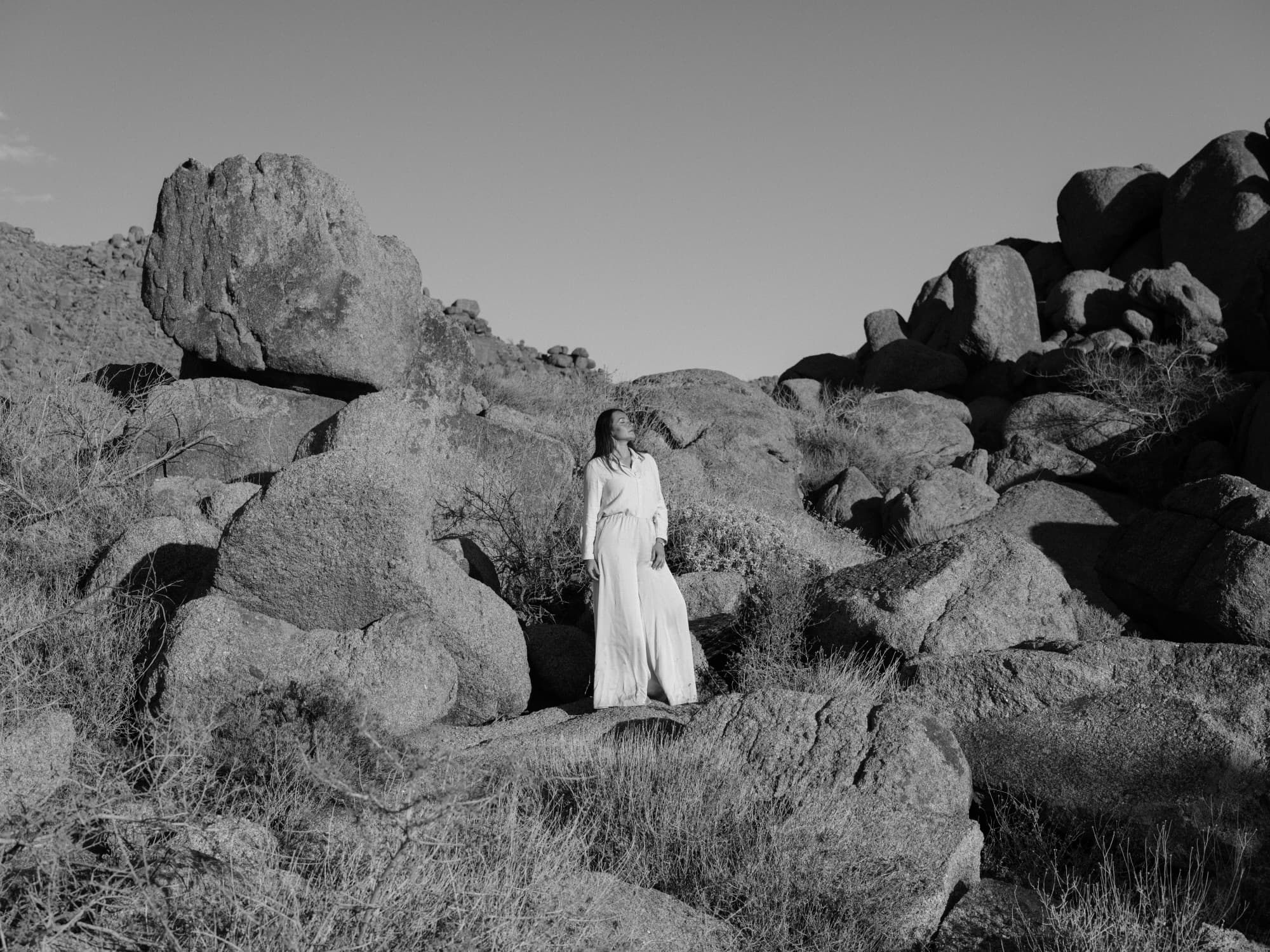 A woman in a long white dress standing among the granite boulders