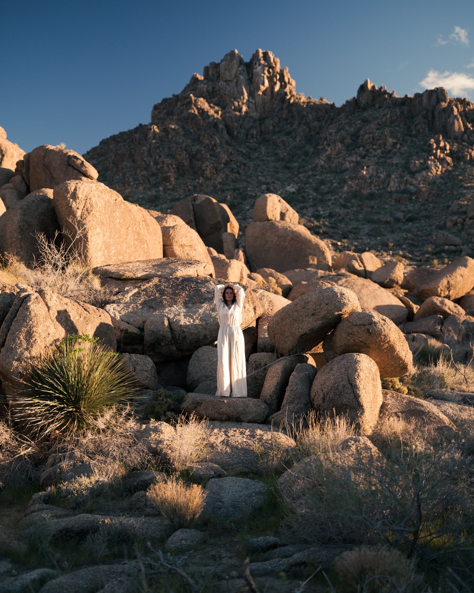 A woman in white standing among the granite boulders beneath the jagged peak