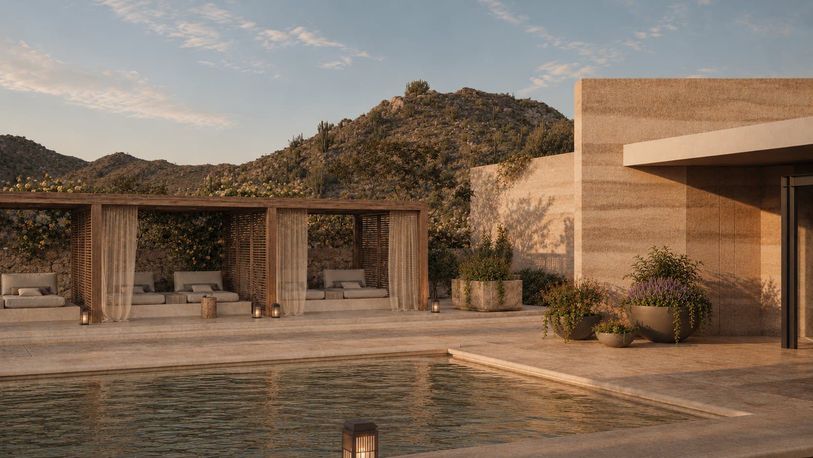 Four open timber cabanas with linen curtains and cushioned daybeds line one side of a pool terrace, with planters and a stone building at right and a cactus-covered hill behind.